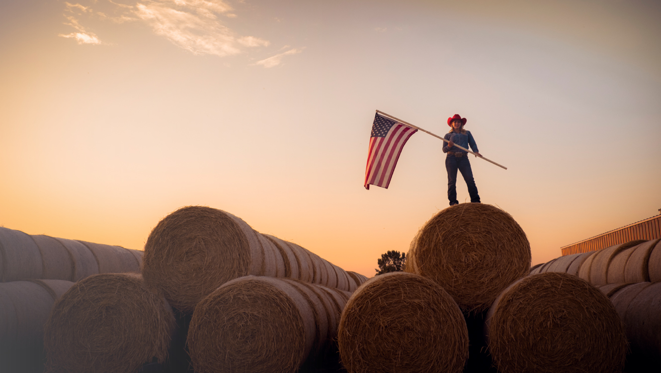 woman standing on hay bales holding US flag